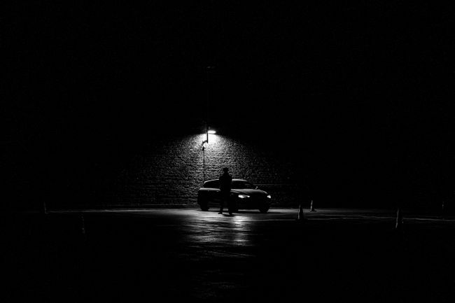 A man standing in front of a lit up car under a bright lamp post in the dark