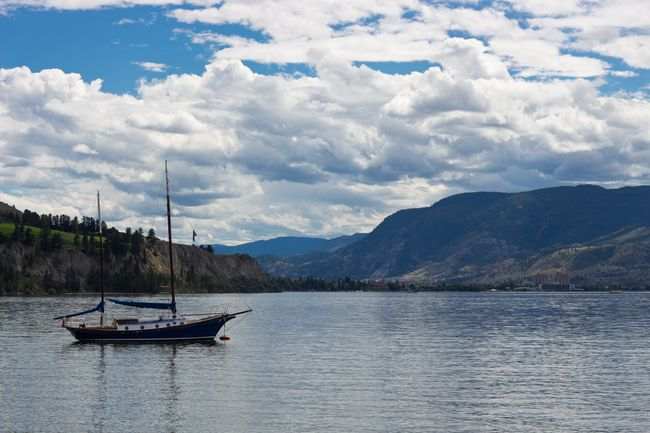 Peaceful scene with a boat on Okanagan Lake, surrounded by mountains and clouds in Kelowna, BC