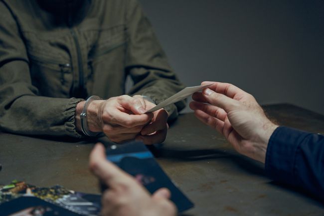 Hands exchanging evidence during an interrogation scene in a dimly lit room